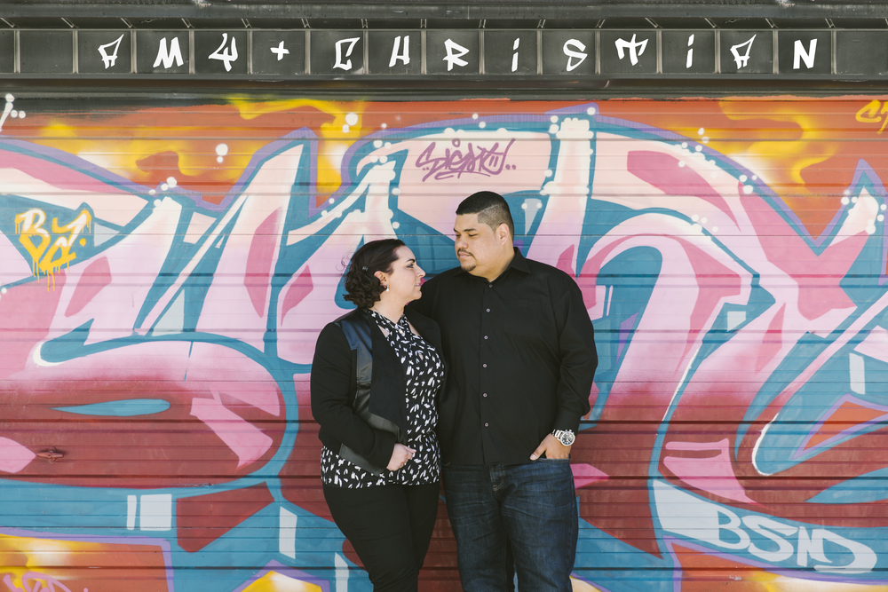   When Amy and Christian told me they met at a bookstore and would like to reflect that part of their relationship in their engagement photos, there was also another part of them that needed to be told as well.  That’s when we decided that shooting in Toronto’s notorious Graffiti Alley would be a great fit in representing their relationship and personalities.  We started the day at a second hand bookstore called Belfour Books on College. The store was filled from top to bottom of shelves full of interesting books on various types of subjects. These two naturally harmonize and complement each other so well that they didn’t even plan on showing up in the same blue inspired matching outfits. That’s how you know they are just made for each other!! Although it wasn’t the exact bookstore of where they met, it ended up being a great backdrop to their engagement photos and an awesome representation of how their love story began. Next we headed down to the Graffiti Alley to continue taking some more pictures.  Although it was quite a bright sunny day, the weather happened to be a little more on the cooler side of spring then we would of preferred.  Luckily, Amy and Christian are two great champs who braved through the cool breezes all for the sake of art!! Since these two prefer city and urban places, Graffiti Alley ended up being a perfect place to capture this side of them. Plus its always great getting to take pictures in an environment that celebrates art and talent. We later walked back up Bathurst to visit this beautiful mural located alongside Alexandria Park.  That’s when Amy and Christian decided to bust out the hilariously adorable matching wedding date shirts Amy’s aunt got them for Christmas. What a fun way to wrap up an adventurous day walking around.  Looking forward to seeing these two again at their wedding!