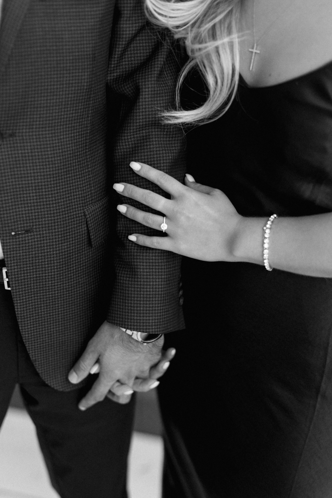 Black and white photo of an engagement ring that the fiance wears while gently holding her fiance's arm