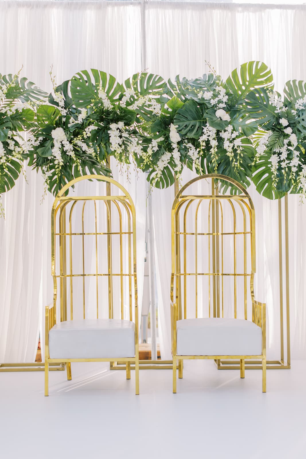 Golden head chairs for a wedding with tropical leafs hanging over the top