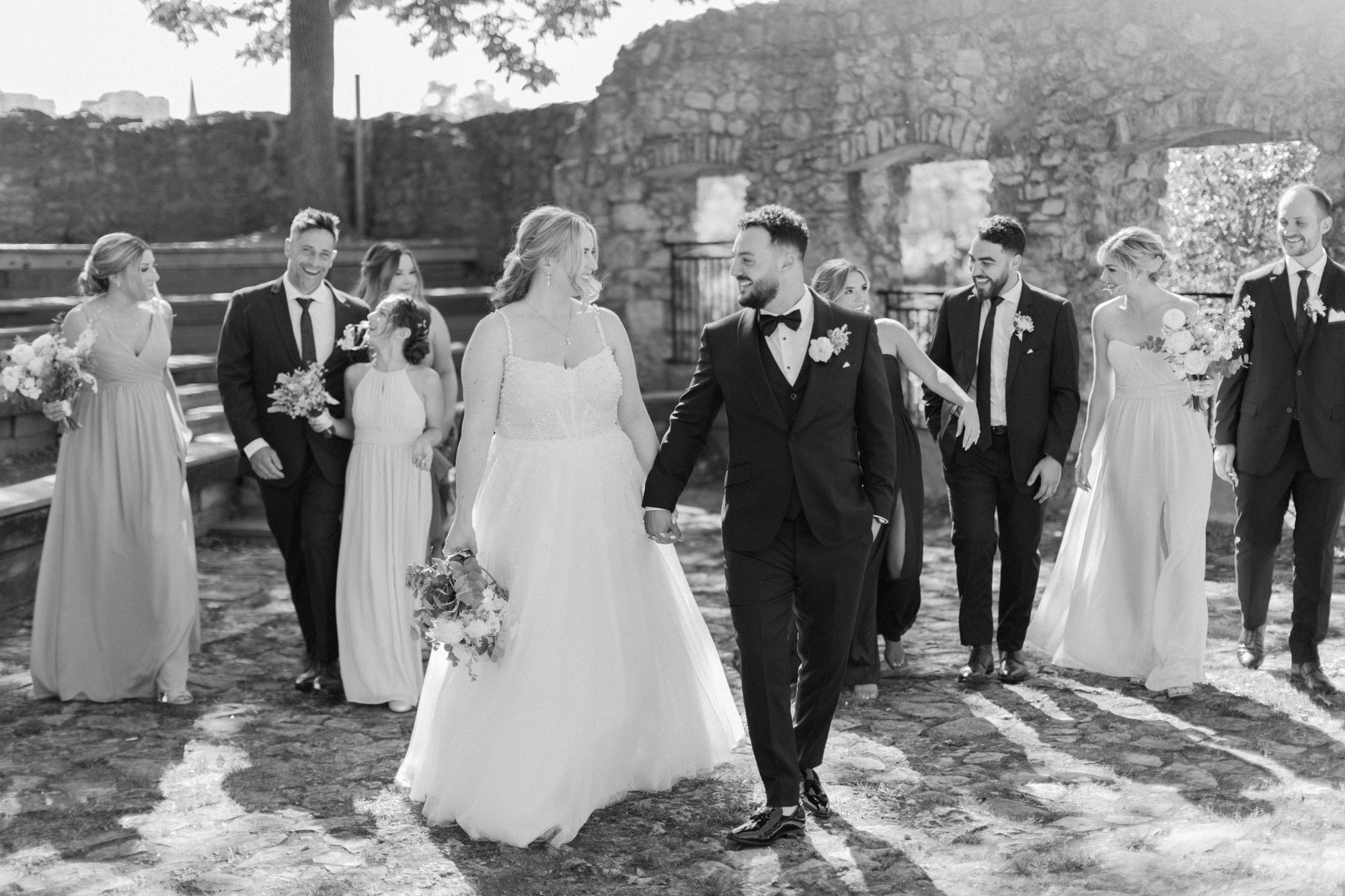 Black and white photo of the bride and groom walking with wedding party at Millrace Park in Cambridge