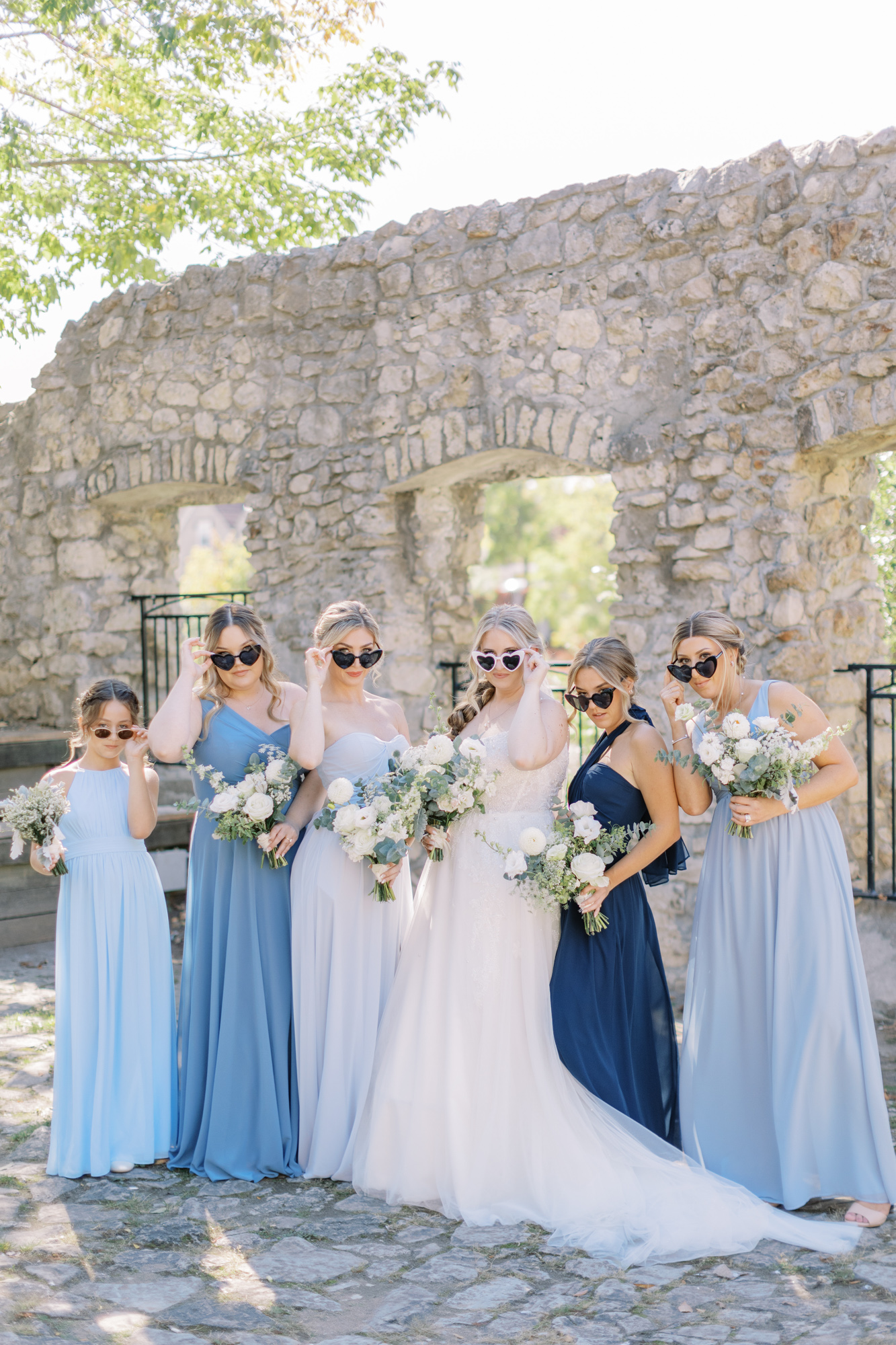 Bride and bridesmaids with heart-shaped sunglasses at Mill Race Park in Cambridge