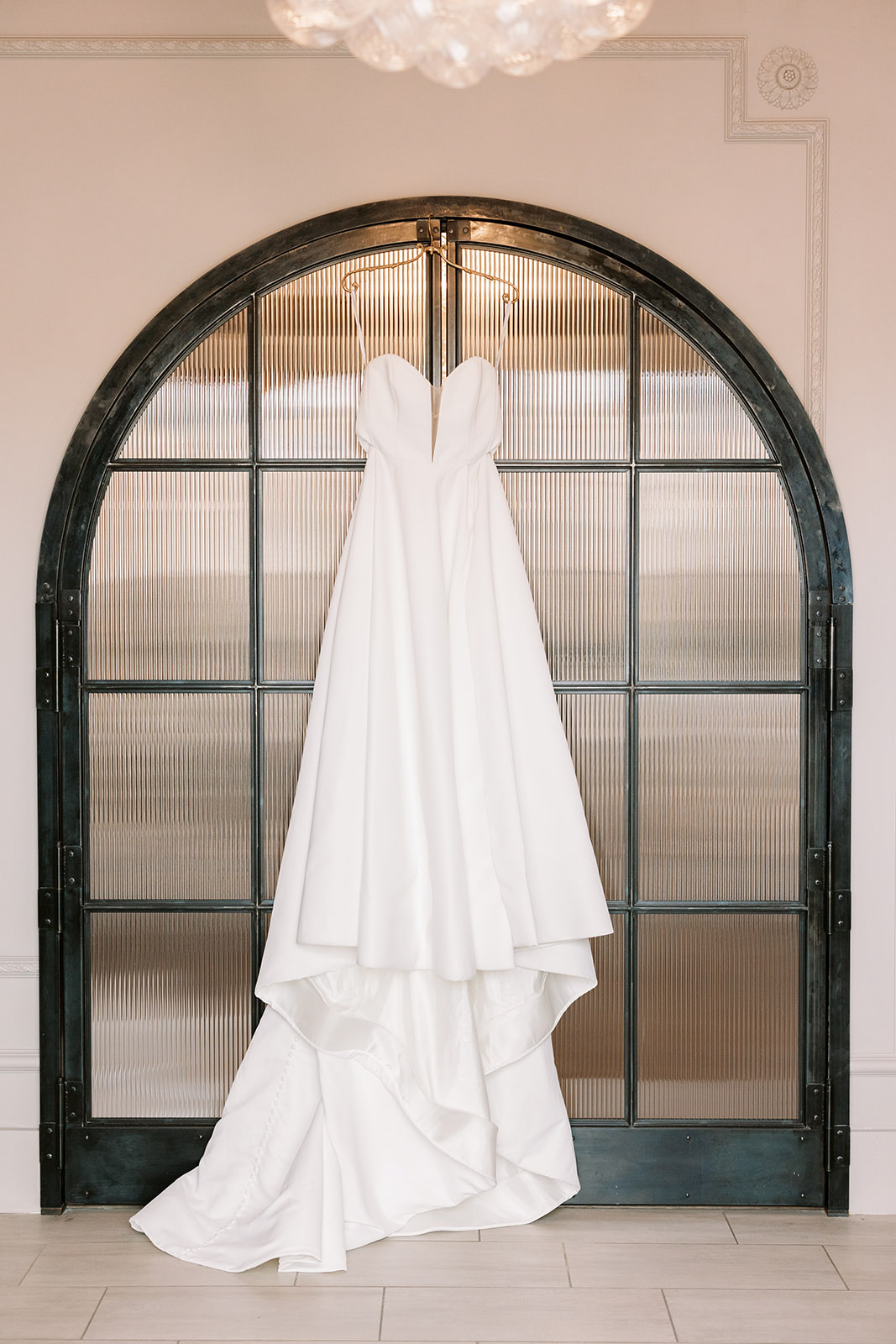 Wedding dress from Sash + Bustle Boutique hanging on modern arched doorway