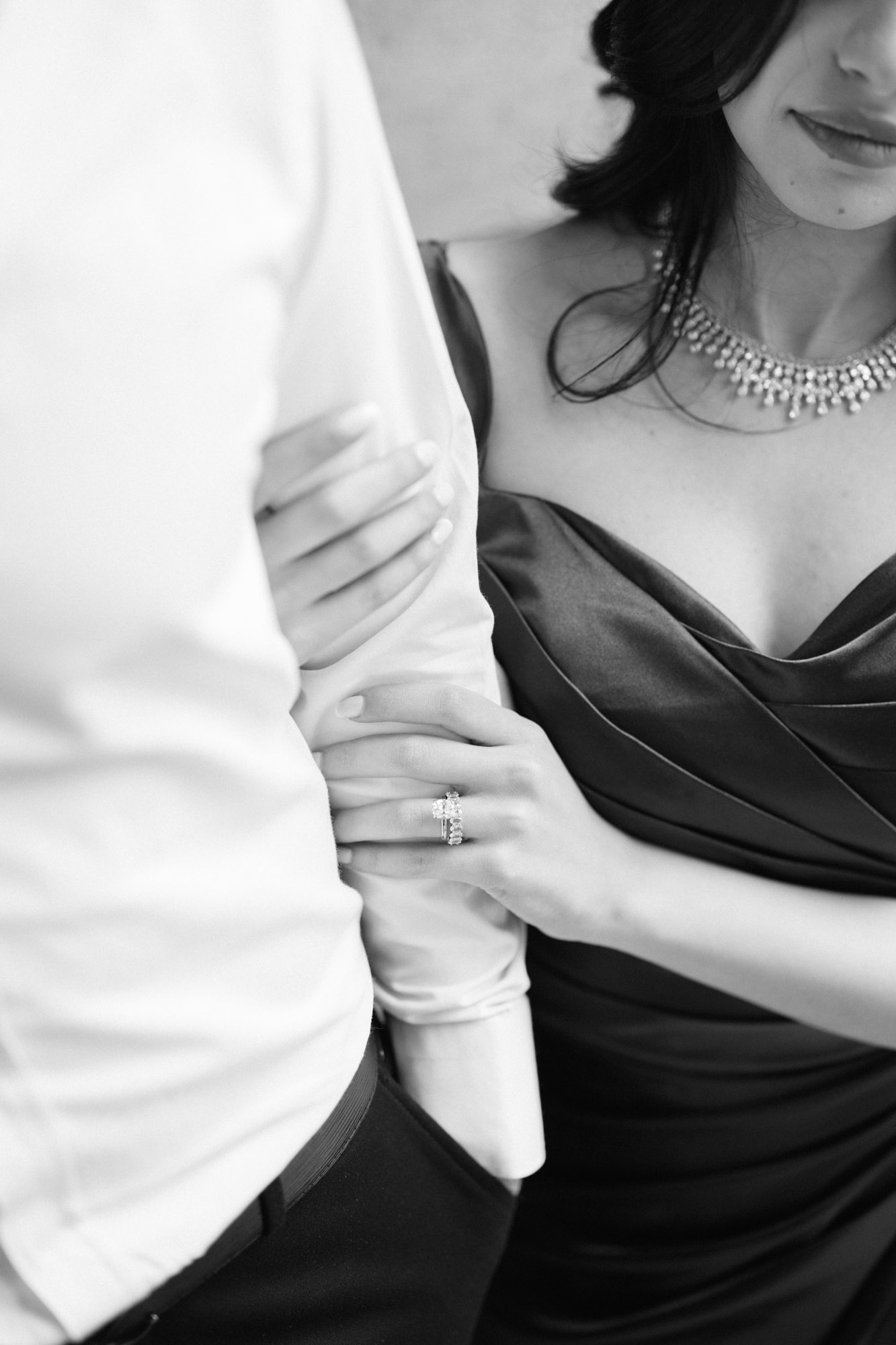 Close up photo of woman holding onto fiancé arm with engagement ring showing